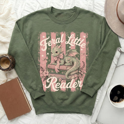 Green sweatshirt with a cute dragon on books, reading "Feral Little Reader."