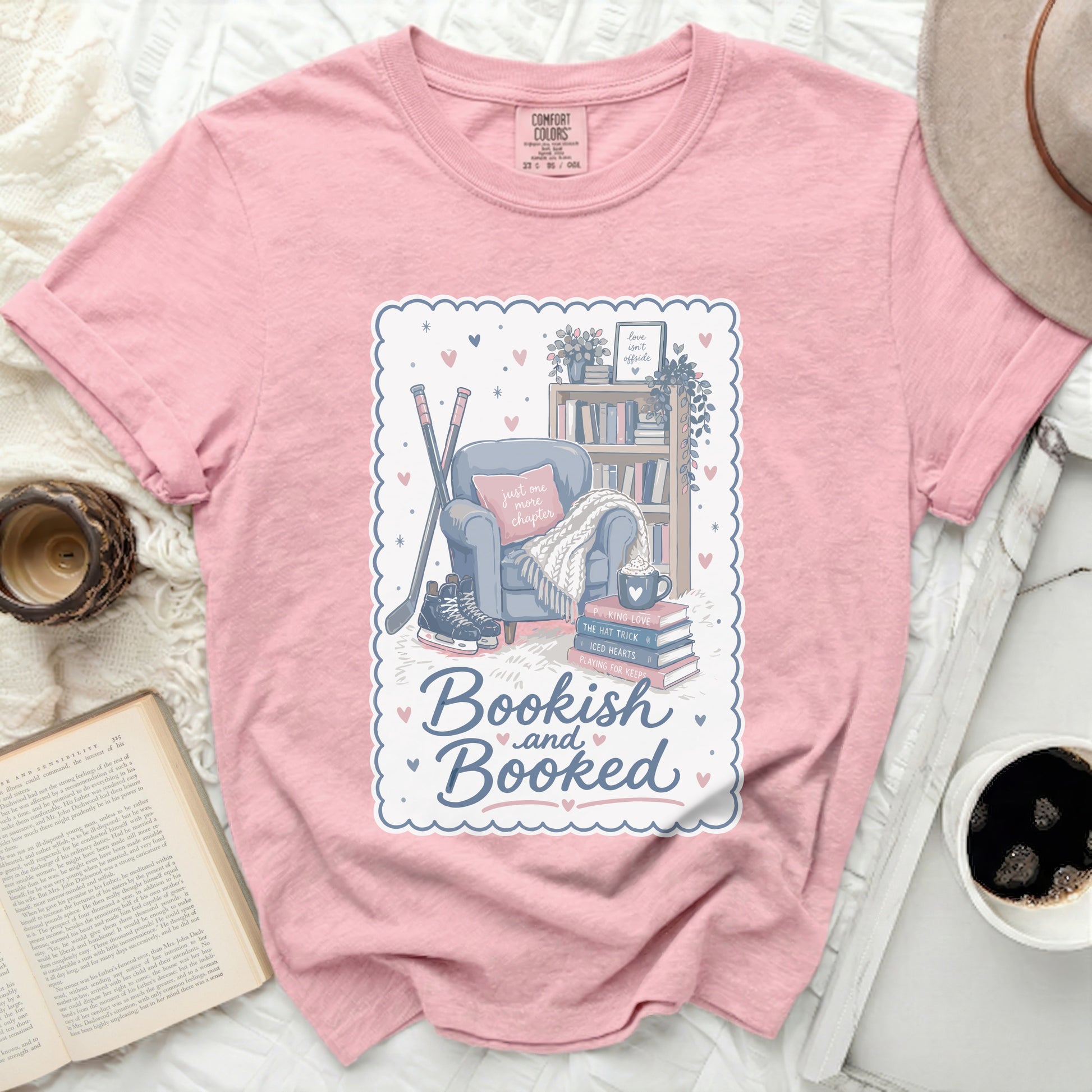Pink t-shirt with "Bookish and Booked" text and reading, hockey, and cozy items.