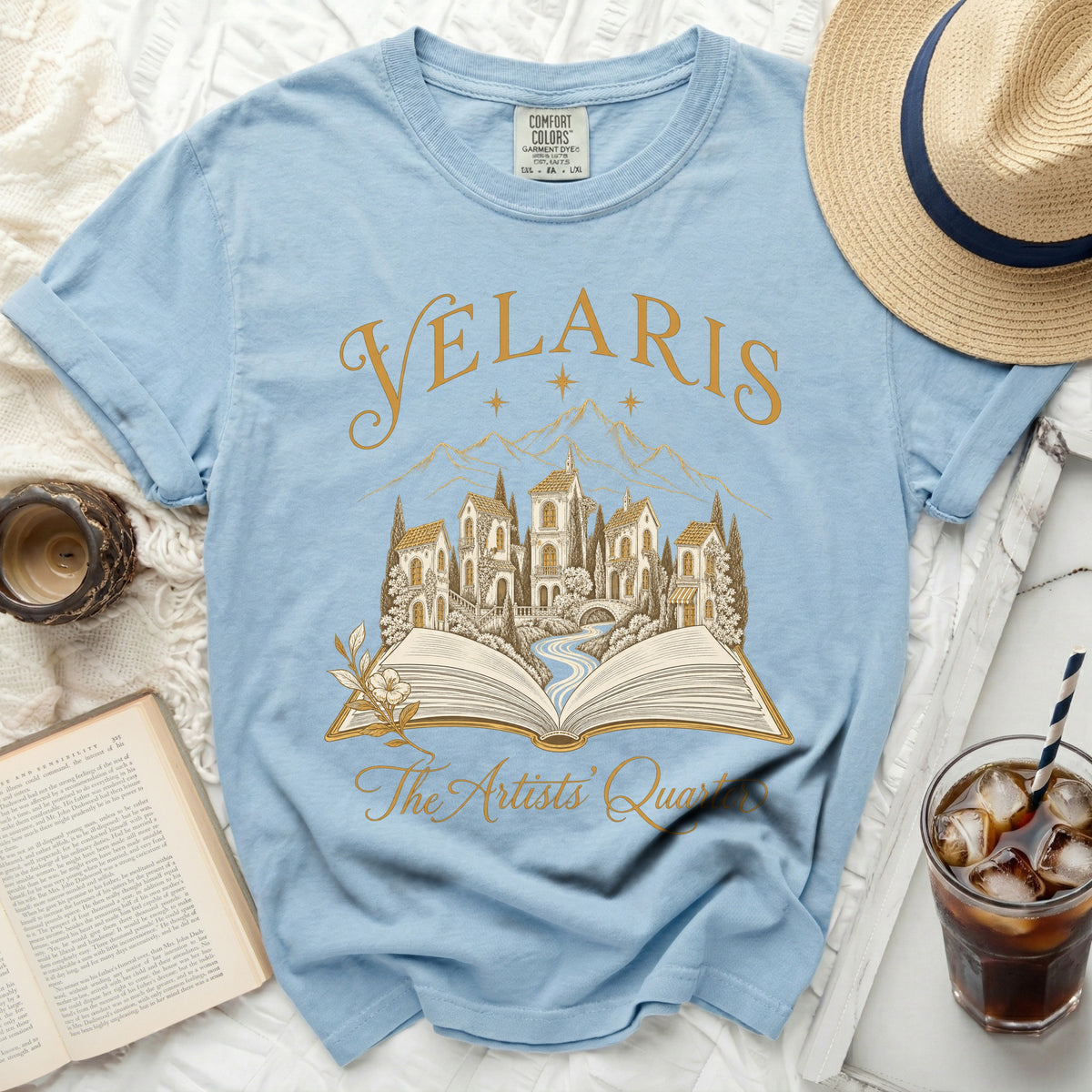 Light blue t-shirt with "Velaris The Artists' Quarter" text and an open book city scene.