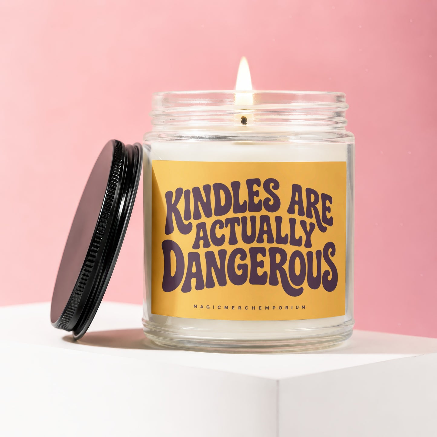 Glass candle with burning wick and yellow label reading "KINDLES ARE ACTUALLY DANGEROUS".