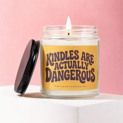 Glass candle with burning wick and yellow label reading "KINDLES ARE ACTUALLY DANGEROUS".