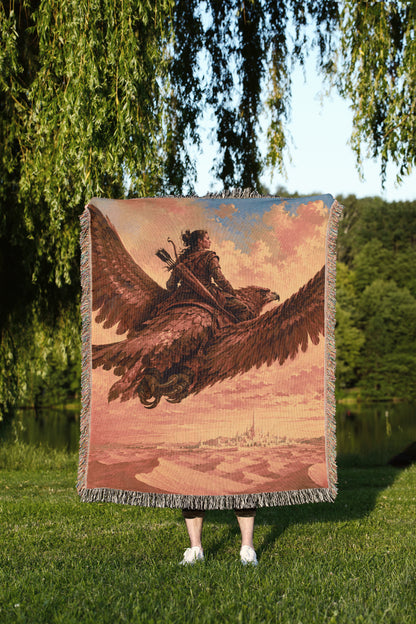 A person is standing in a grassy area, holding a large tapestry or blanket that features a painting of a person riding a winged creature, possibly a dragon or a mythical bird.