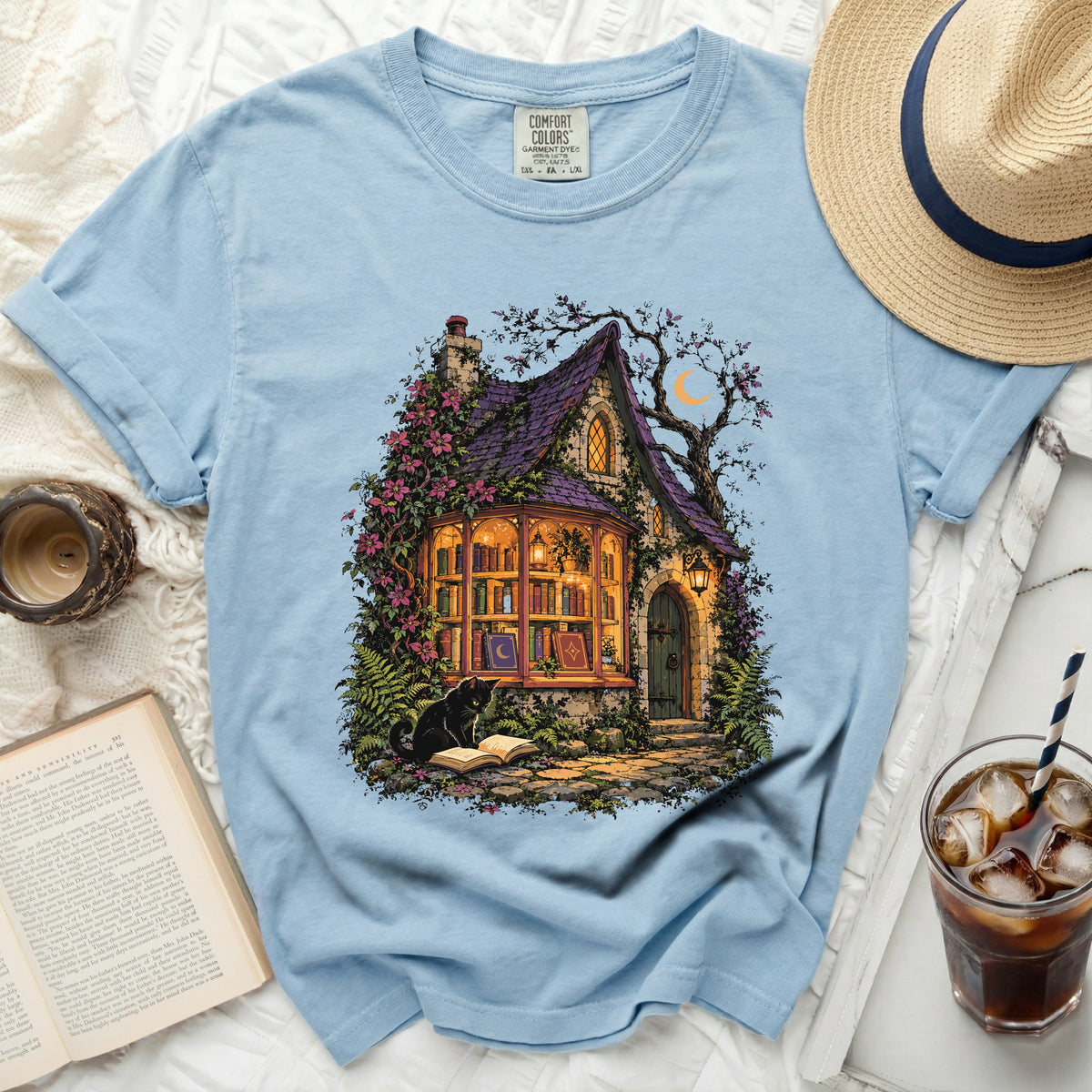 Light blue t-shirt with a whimsical witch's cottage and black cat graphic.