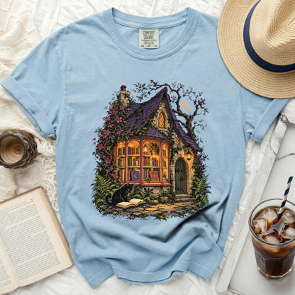 Light blue t-shirt with a whimsical witch's cottage and black cat graphic.