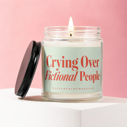 Candle with lit wick, glass jar, black lid, and mint green label reading "Crying Over Fictional People".