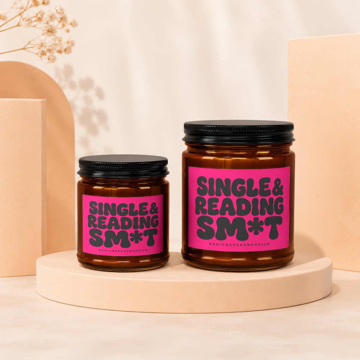 Two amber glass candles with black lids on display pedestals, featuring bright pink labels.