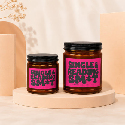 Two amber glass candles with black lids on display pedestals, featuring bright pink labels.