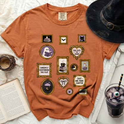 Orange t-shirt with framed Halloween-themed illustrations including a ghost reading, a cat, and spooky phrases.
