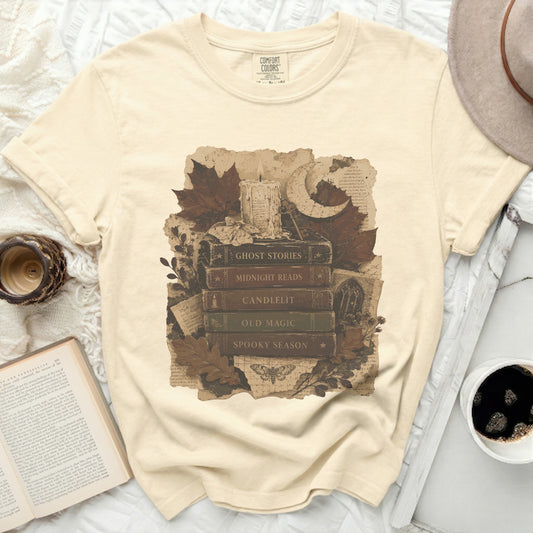 T-shirt with stack of books, candle, moon, and autumn leaves graphic.