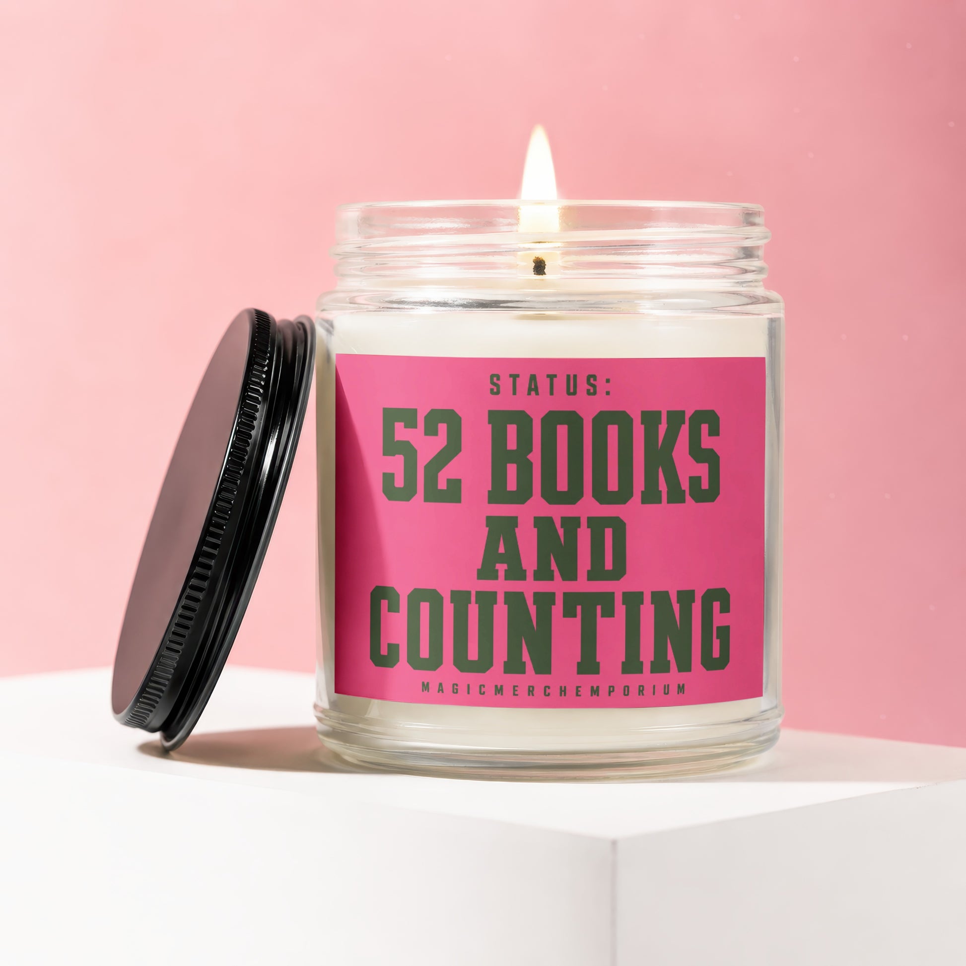 Lit candle in a glass jar with a pink label reading "STATUS: 52 BOOKS AND COUNTING"
