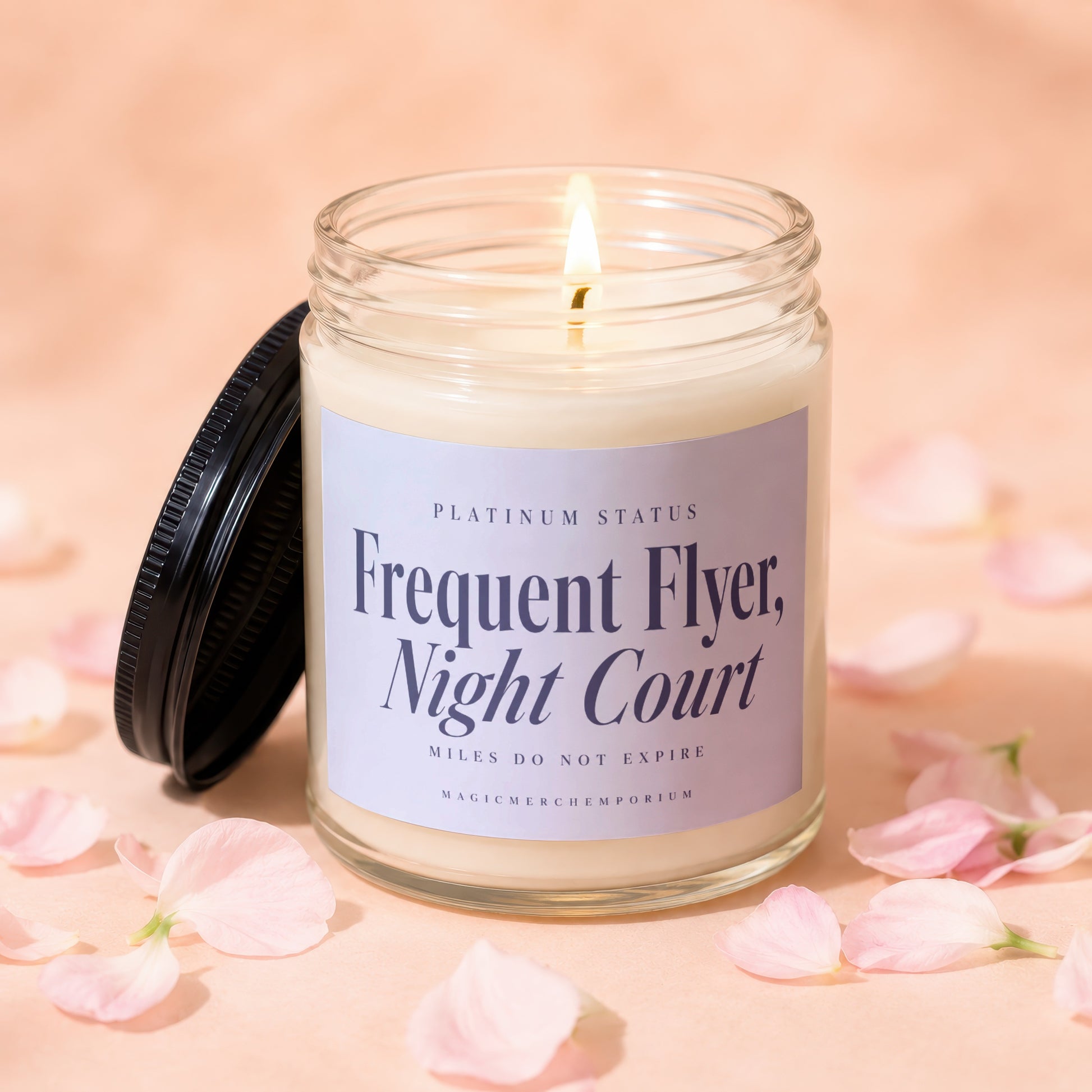 Lit candle in a glass jar with a black lid and pink petals scattered around it.