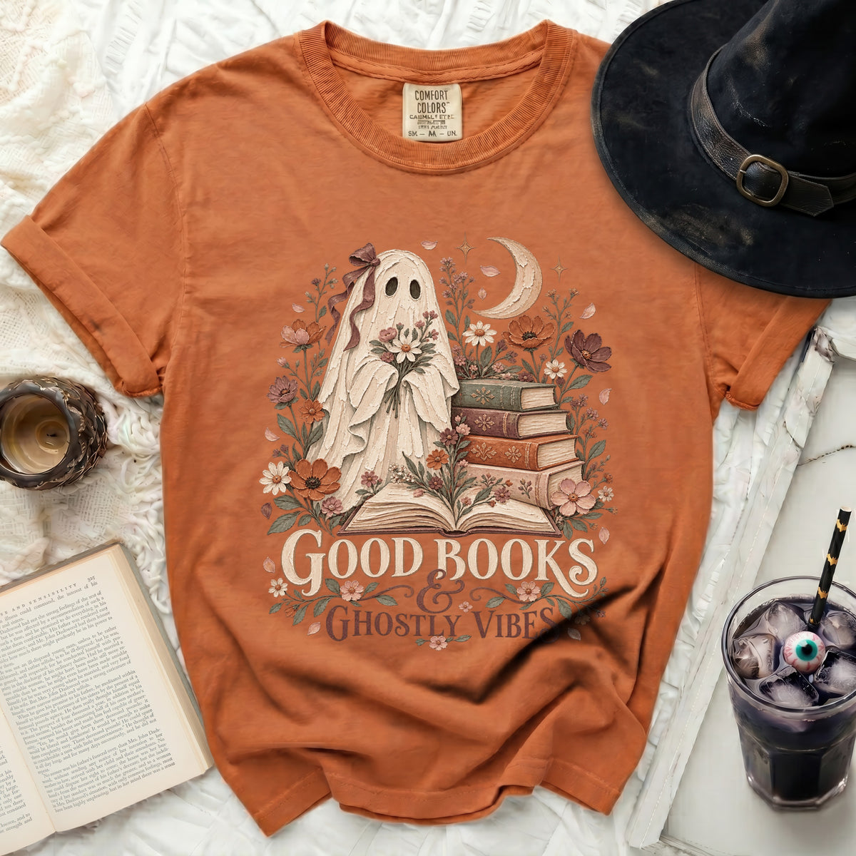 Orange t-shirt with a ghost holding flowers, books, and the text "Good Books Ghostly Vibes".