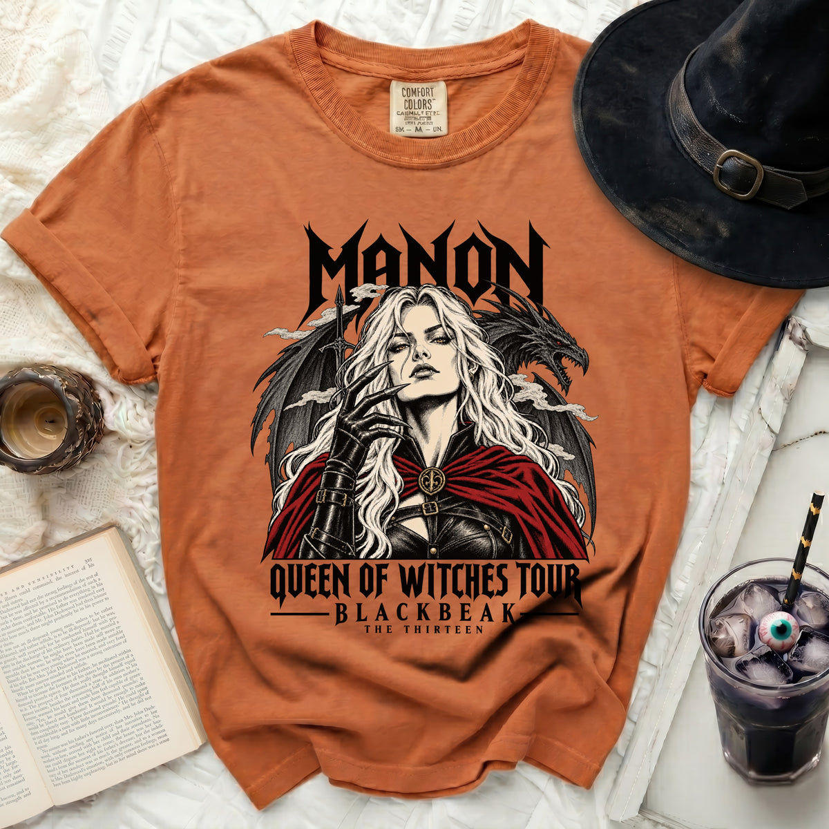 Orange t-shirt with "MANON QUEEN OF WITCHES TOUR BLACKBEAK THE THIRTEEN" graphic.