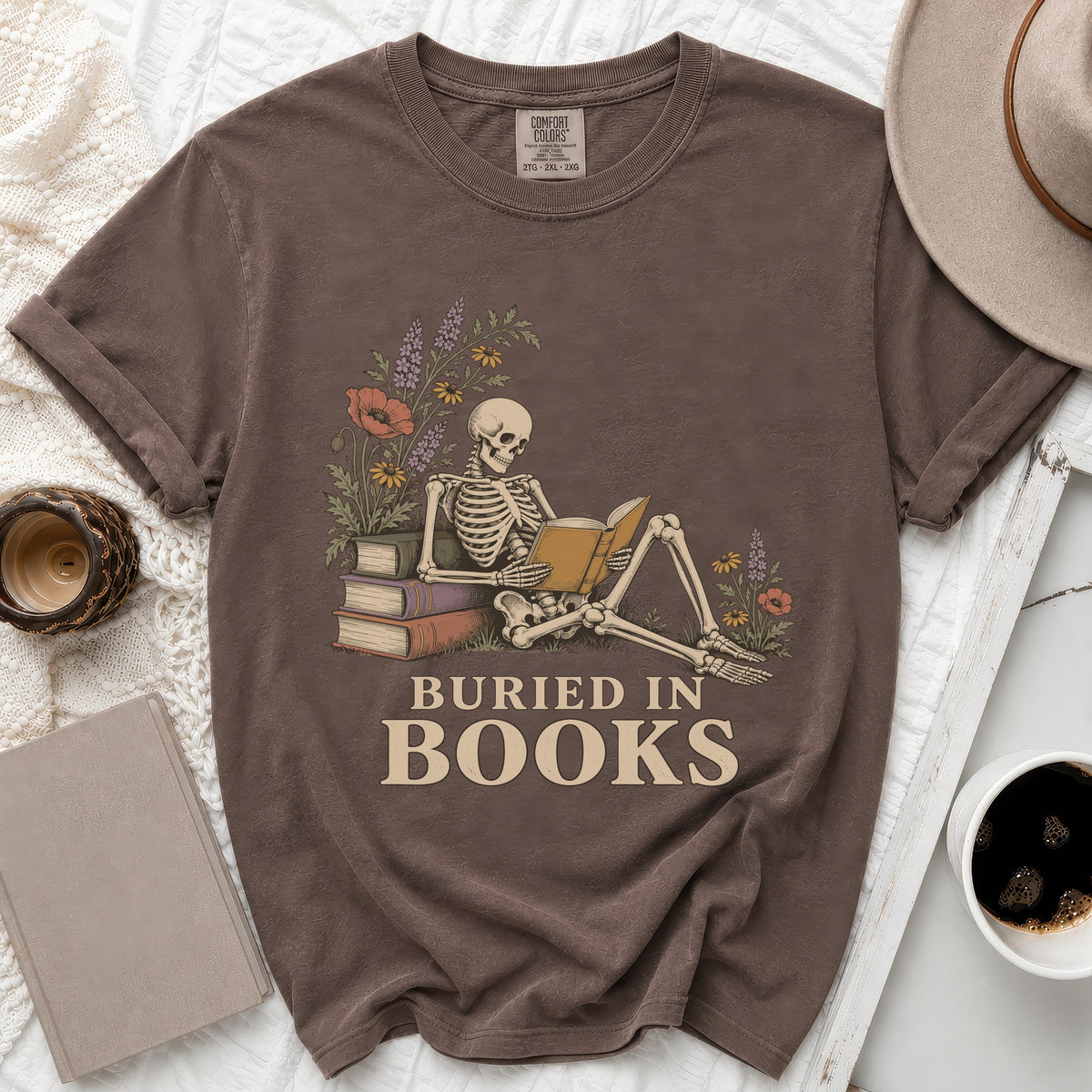 Skeleton reading a book with flowers and text "BURIED IN BOOKS".
