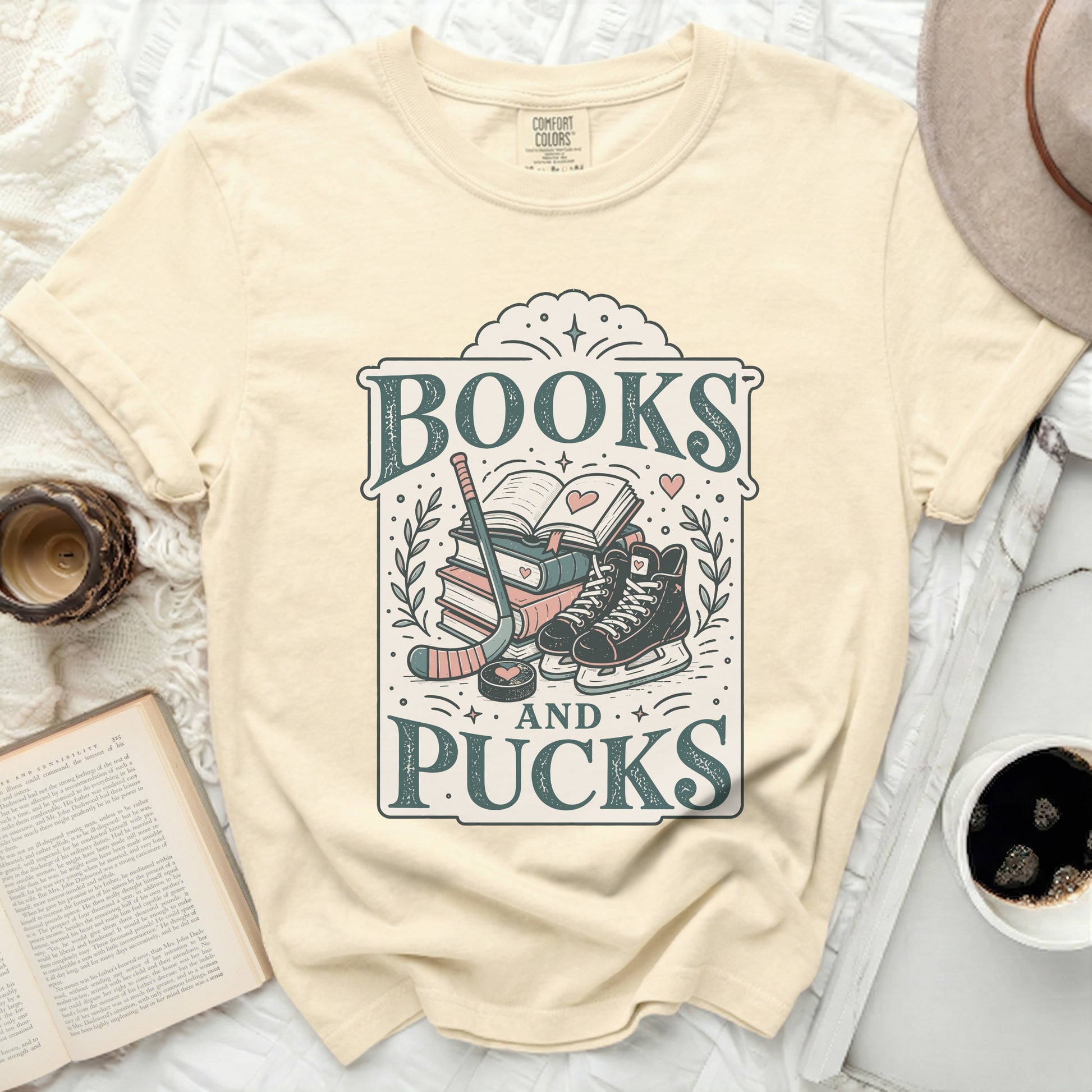 Comfort Colors t-shirt with "Books and Pucks" text, hockey gear, and ice skates.