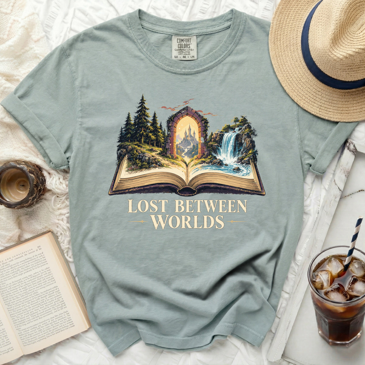 T-shirt with open book graphic showing fantasy castle through arched portal and text LOST BETWEEN WORLDS.