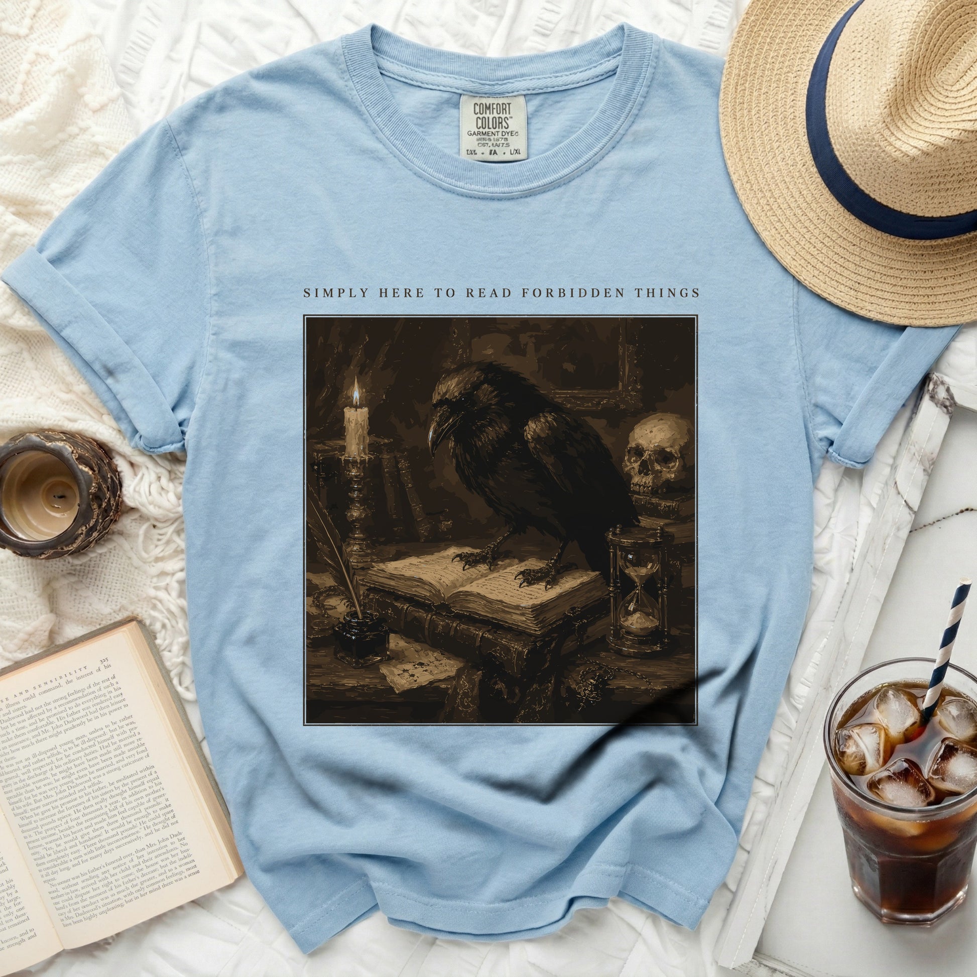 Light blue t-shirt with raven illustration and text "SIMPLY HERE TO READ FORBIDDEN THINGS".