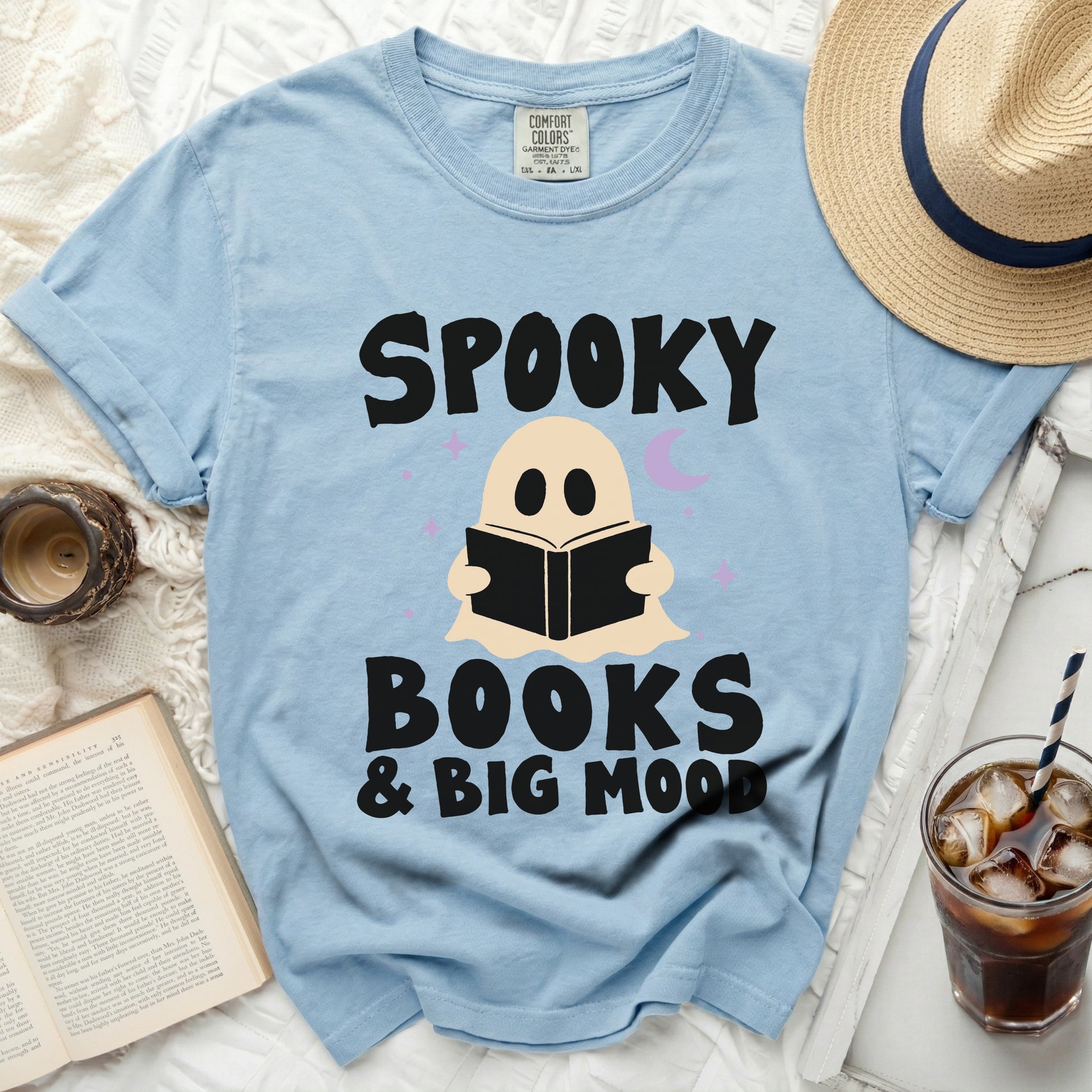 Light blue graphic t-shirt with ghost, book, moon, and stars reading "Spooky Books & Big Mood"