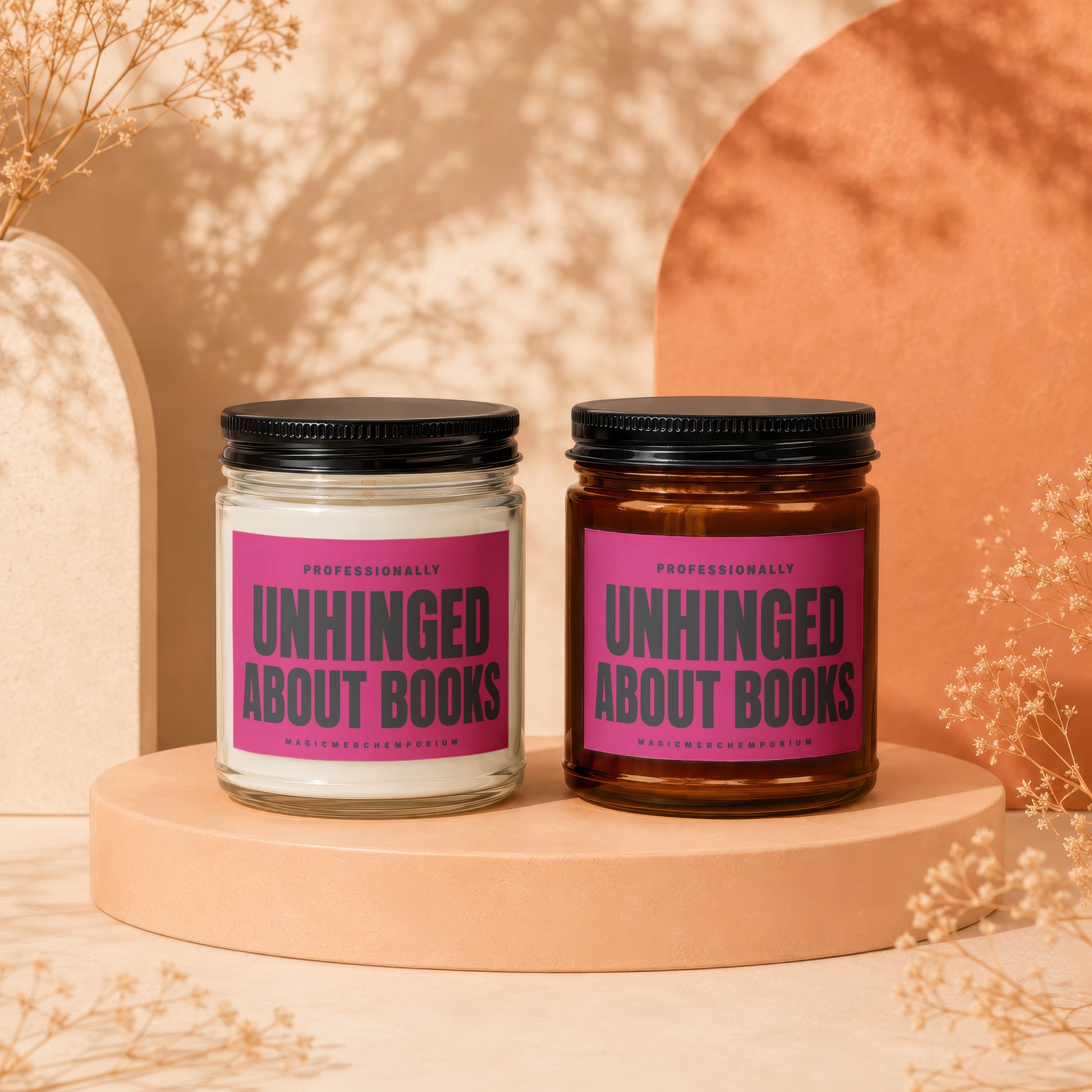 Two candles with pink labels that say "Unhinged About Books" and "MagicMerch Emporium".