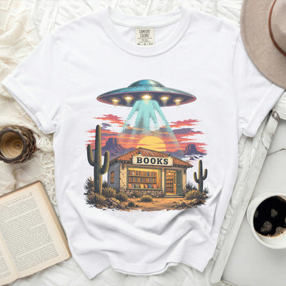 UFO beams light onto a desert book store with a sunset and cacti.
