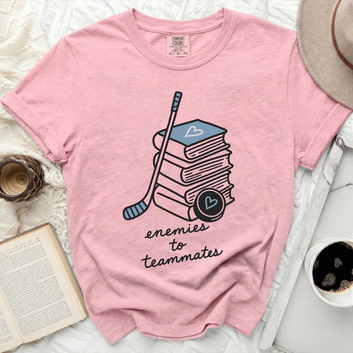 Pink t-shirt with books, hockey stick, and puck; text "enemies to teammates."