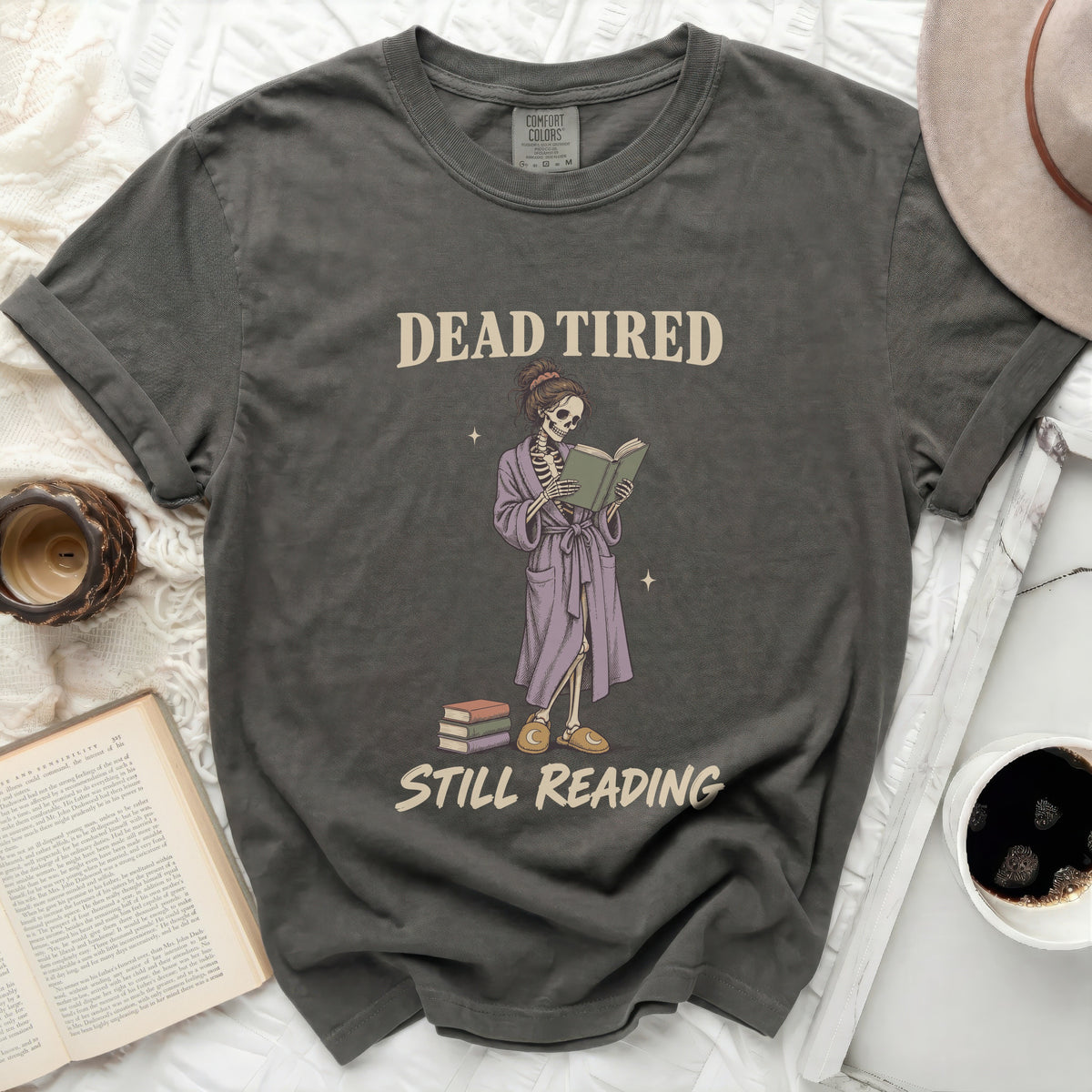 T-shirt with skeleton reading a book with text "DEAD TIRED STILL READING".