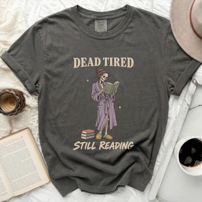 T-shirt with skeleton reading a book with text "DEAD TIRED STILL READING".