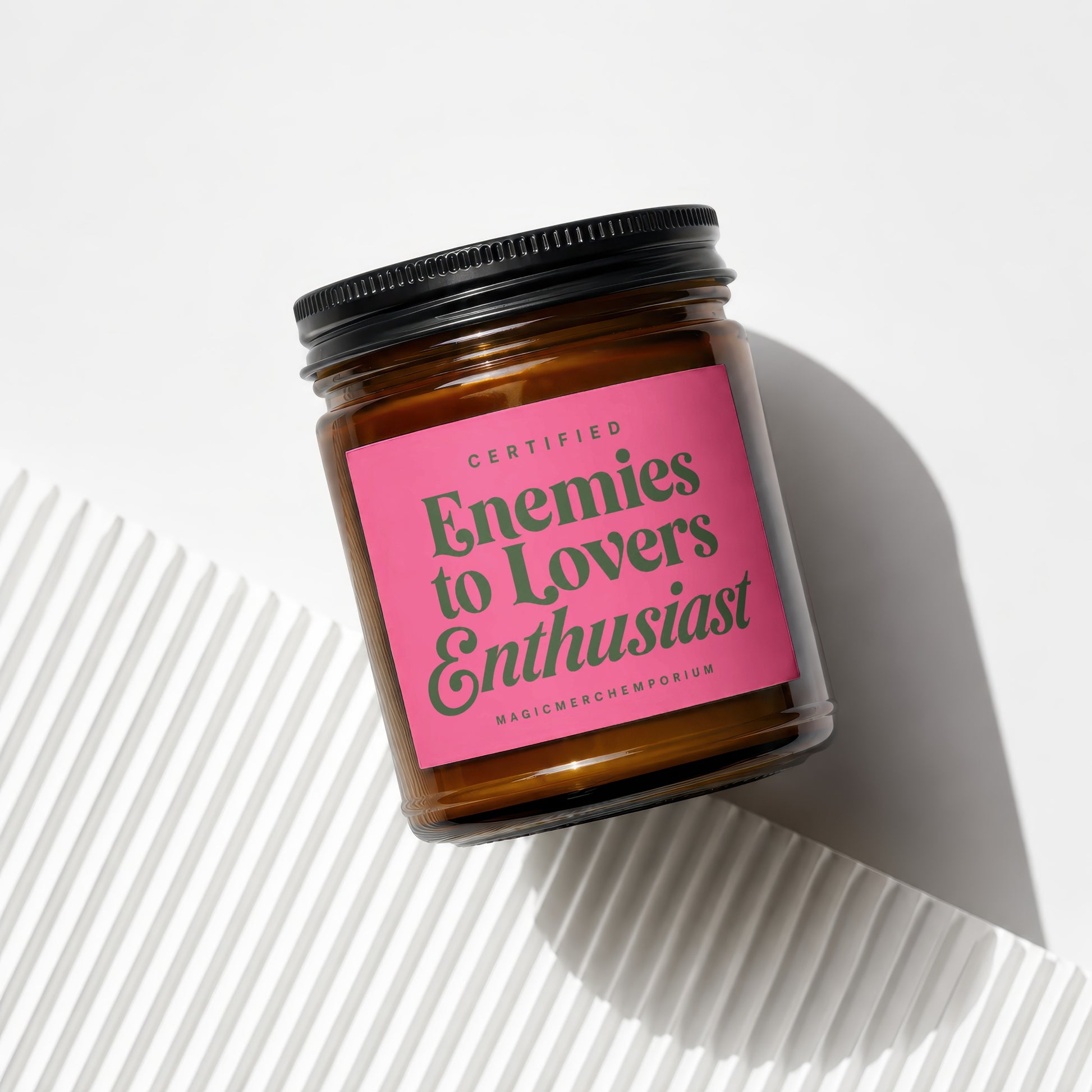 Amber jar candle with "Certified Enemies to Lovers Enthusiast" pink label and black lid.