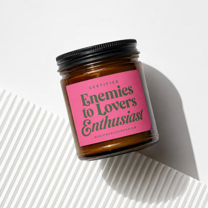 Amber jar candle with "Certified Enemies to Lovers Enthusiast" pink label and black lid.
