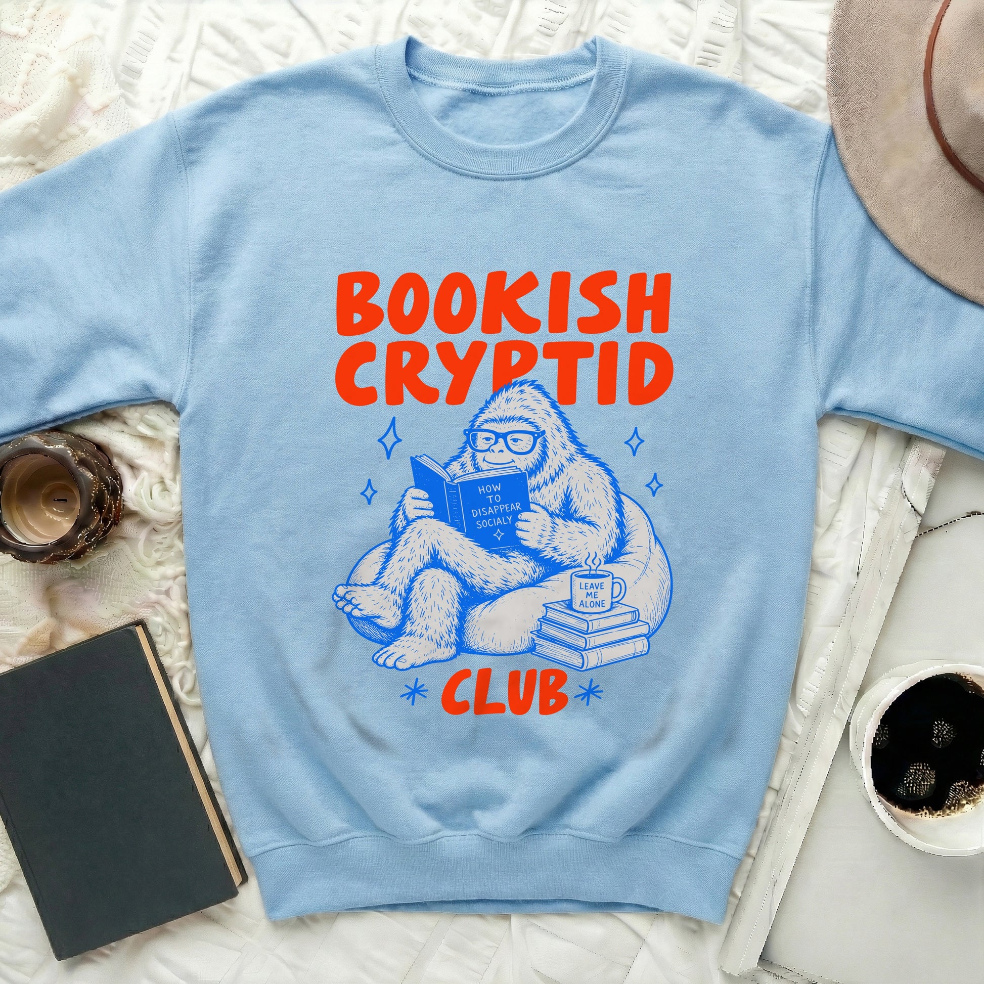 Light blue sweatshirt with "Bookish Cryptid Club" text and illustration of Bigfoot reading.