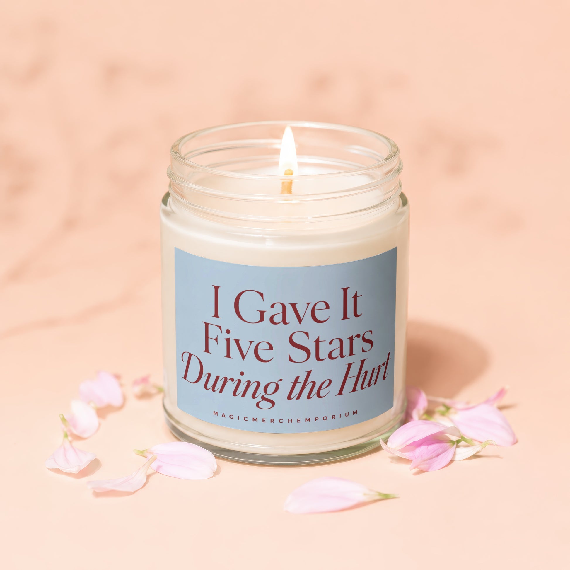 Lit jar candle with blue label reading "I Gave It Five Stars During the Hurt", surrounded by petals.
