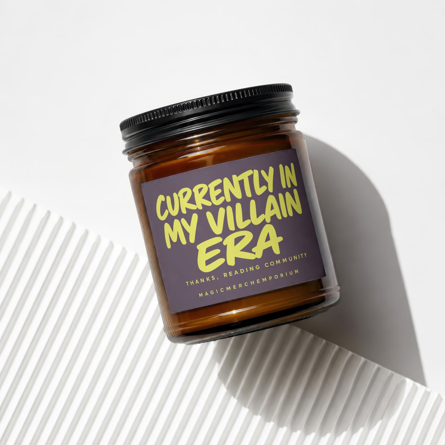 Amber glass candle labeled "Currently in my Villain Era" with "MagicMerchEmporium" below.
