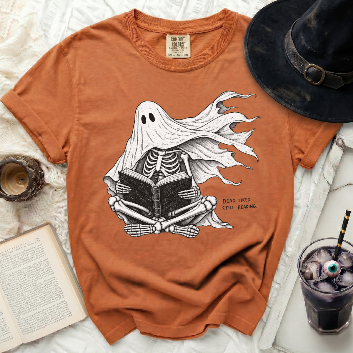 Orange t-shirt with skeleton ghost reading a book and text "DEAD TIRED. STILL READING."