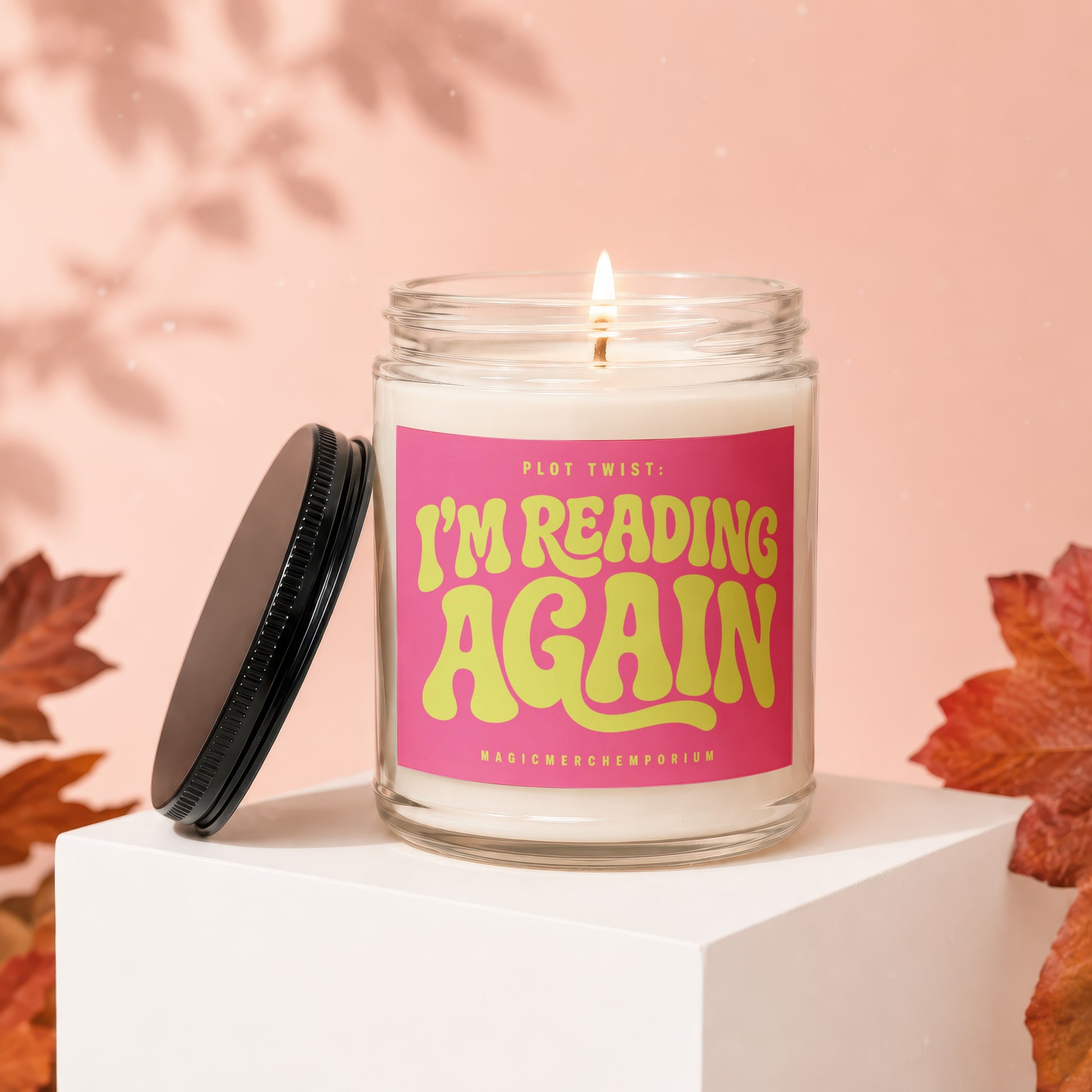 Glass candle with a lit wick and a pink label that reads "PLOT TWIST: I'M READING AGAIN".