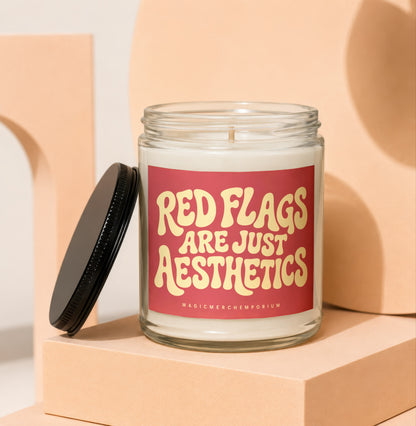 Glass candle with red label reading "Red Flags Are Just Aesthetics".