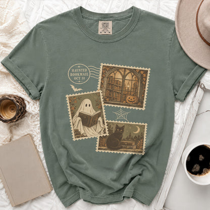 Green t-shirt with Halloween-themed postage stamps: ghost reading, library, black cat, and pumpkin.