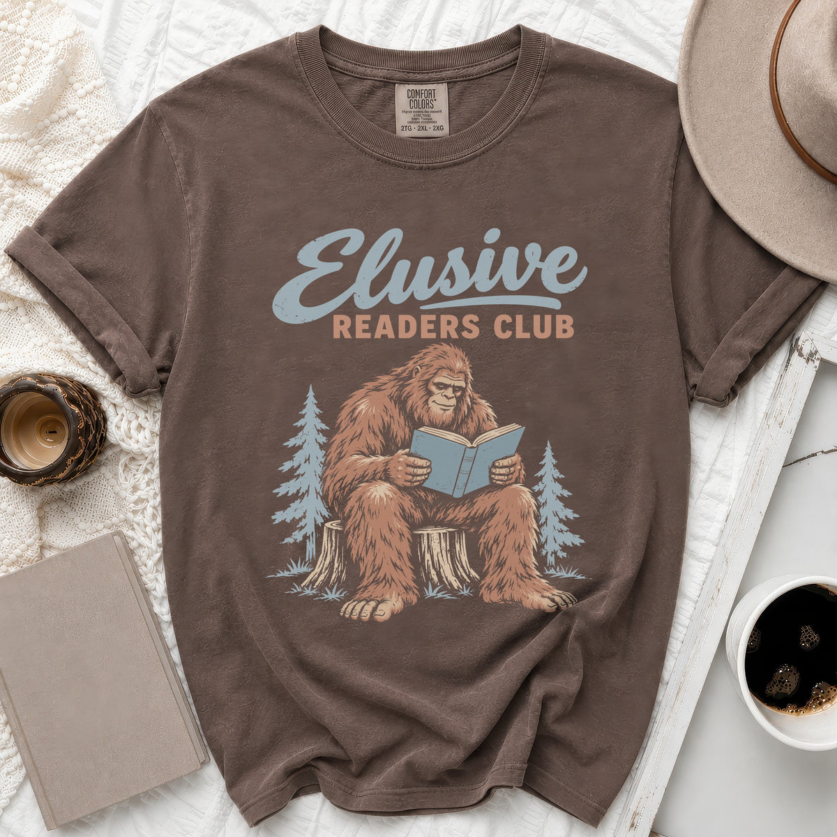 Brown t-shirt with Bigfoot reading a book and text "Elusive Readers Club".