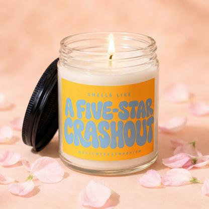 Lit candle in glass jar with "A FIVE-STAR CRASHOUT" on orange label.