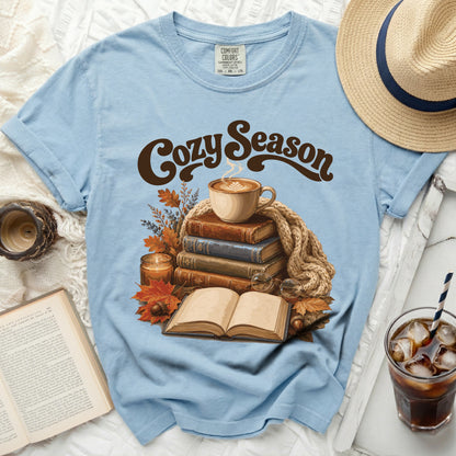Light blue t-shirt with "Cozy Season" graphic, books, coffee, and fall leaves.