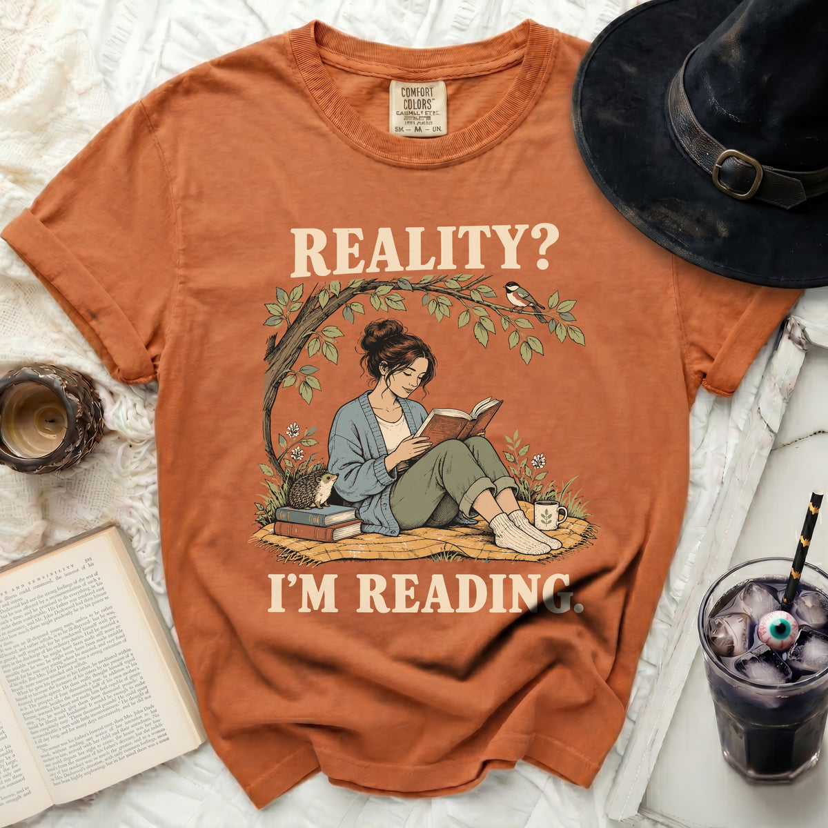 Orange t-shirt with graphic of woman reading under tree, text "REALITY? I'M READING."