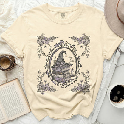 Cream t-shirt with a framed "book of spells" graphic featuring a witch's hat and books.