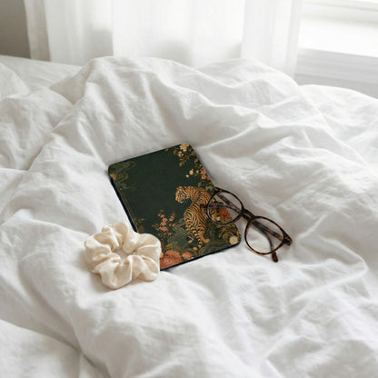 Dark green journal with tiger and floral design, glasses, and scrunchie on white sheets.