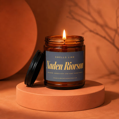 Lit candle in amber jar labeled "Xaden Riorson" on an orange pedestal.