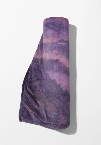 Rolled purple blanket with a mountain landscape print.