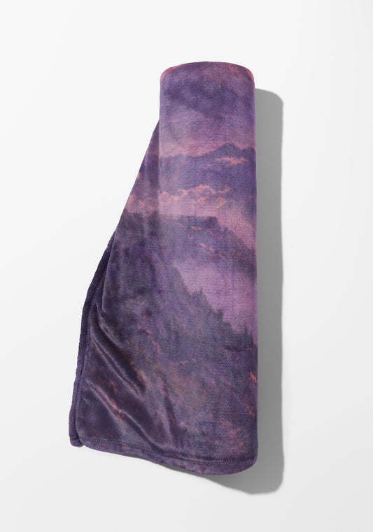 Rolled purple blanket with a mountain landscape print.