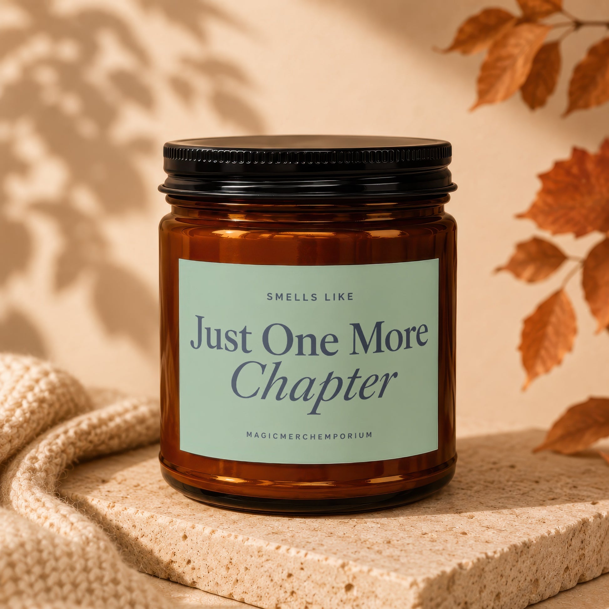 Amber candle labeled "Smells Like Just One More Chapter" on textured surface.