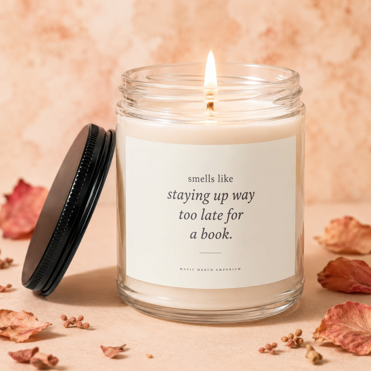 Glass candle with lit wick and label reading "smells like staying up way too late for a book."
