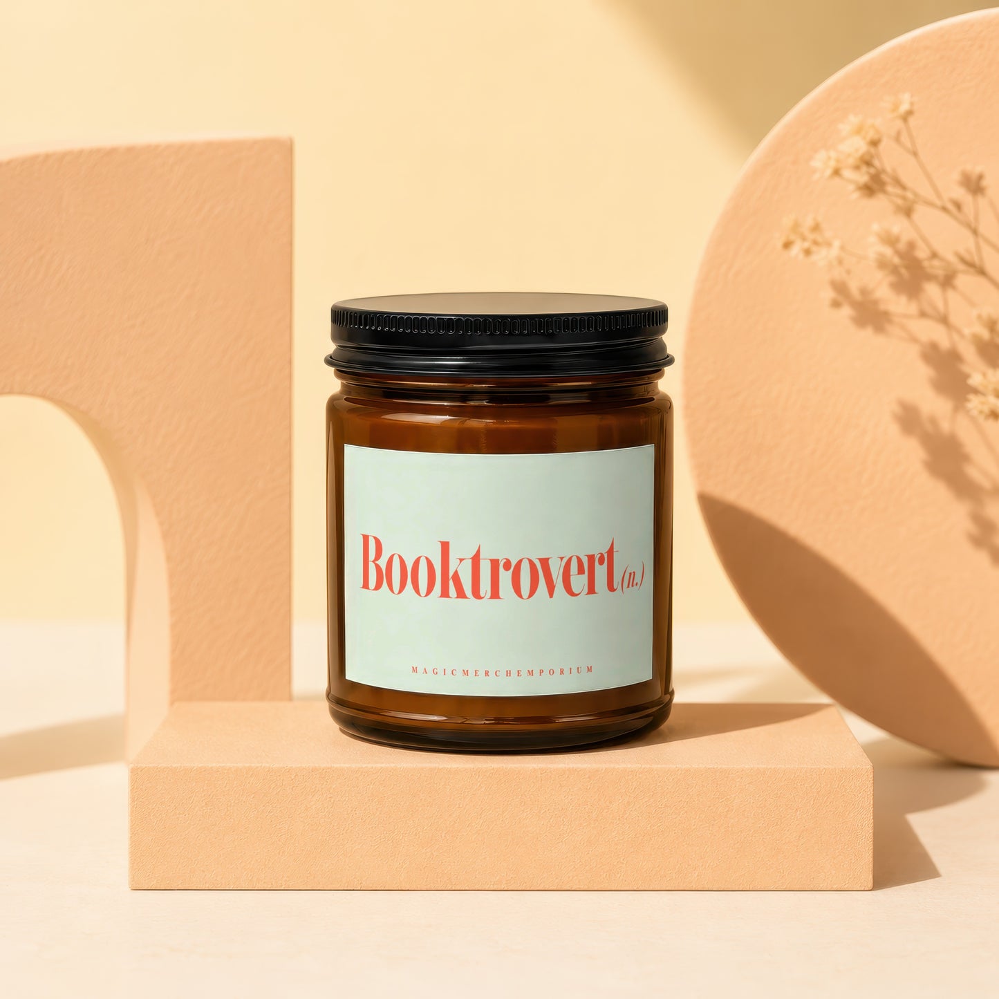 Amber glass candle with "Booktrovert (n.)" and "MAGIC MERCH EMPORIUM" text.