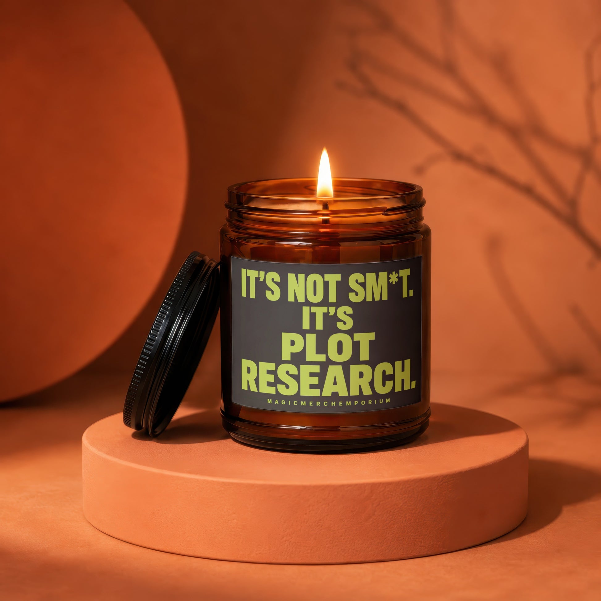 Amber glass candle with lit wick and lid nearby, reads "It's not sm*t. It's plot research."