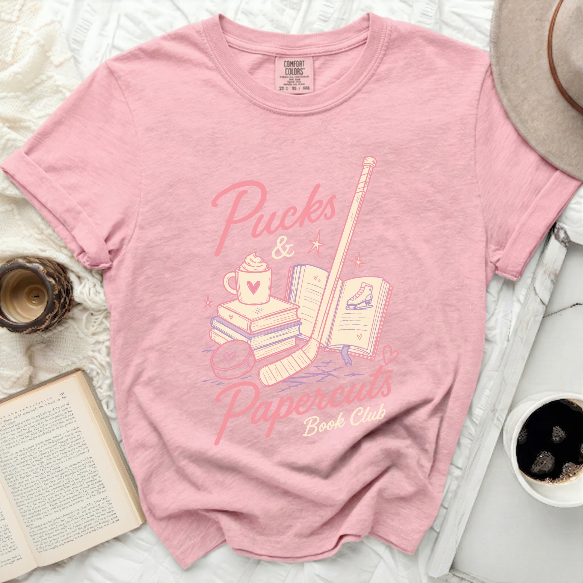 Pink t-shirt with "Pucks & Papercuts Book Club" text and hockey icons.